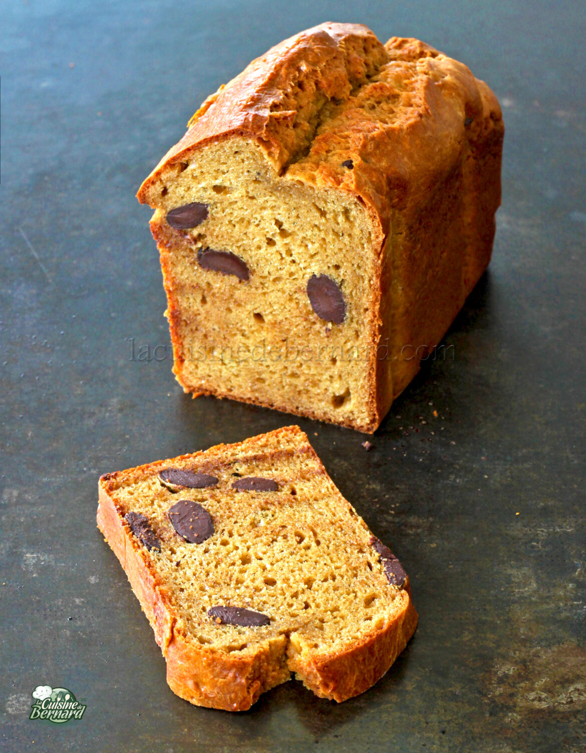 Une miche de pain avec une tranche coupée, montrant des olives cuites à l'intérieur, est posée sur une surface sombre ressemblant à une variante savoureuse du gâteau banane.