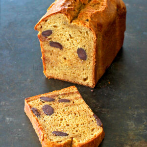 Une miche de pain avec une tranche coupée, montrant des olives cuites à l'intérieur, est posée sur une surface sombre ressemblant à une variante savoureuse du gâteau banane.