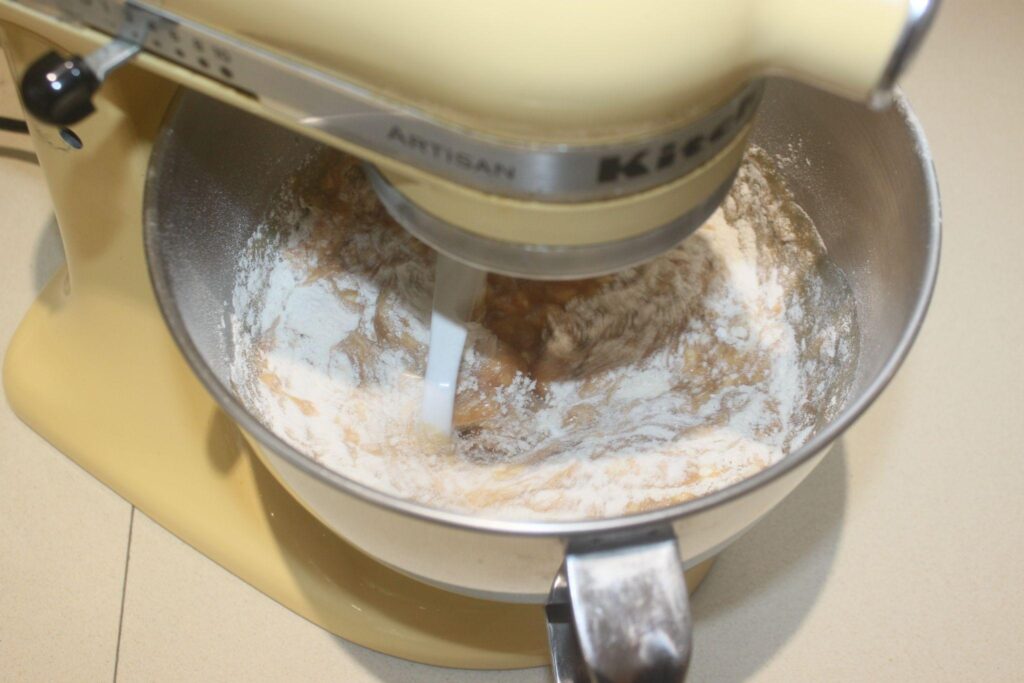 Un batteur sur socle mélangeant de la farine et d'autres ingrédients dans un bol en acier inoxydable sur un comptoir de cuisine.