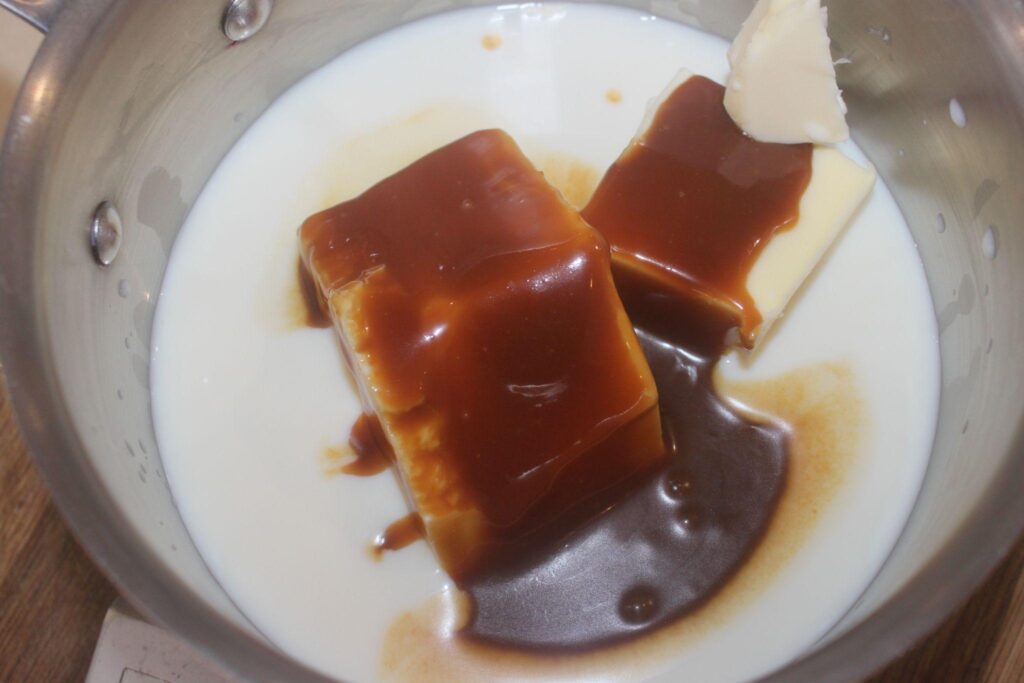 Une casserole contenant du lait, deux bâtons de beurre et du caramel liquide brun ou de la sauce en cours de préparation pour la cuisson.