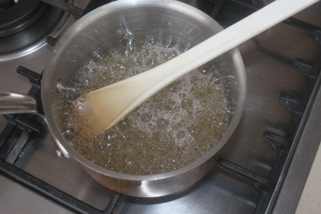 Une casserole contenant un liquide bouillonnant est remuée avec une spatule blanche sur une cuisinière.